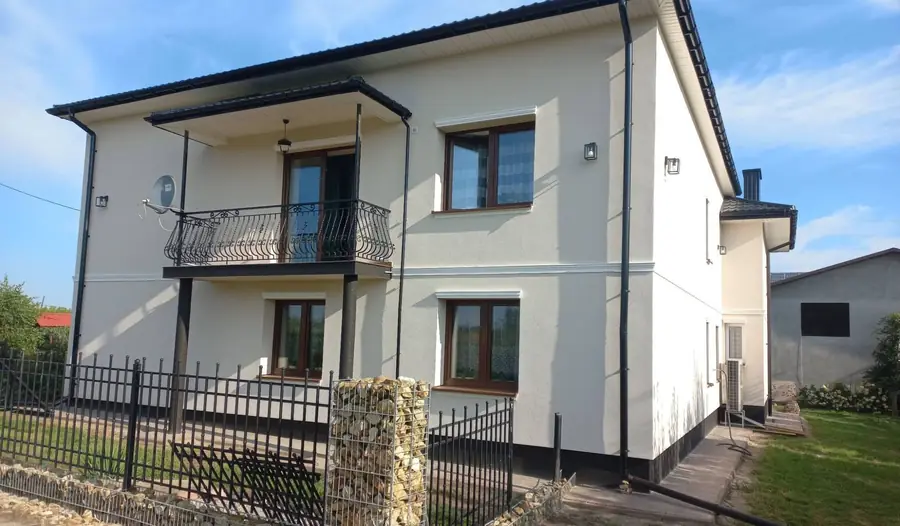 Piętrowy dom z elewacją w ciepłym, łososiowym kolorze i balkonem z kutą balustradą